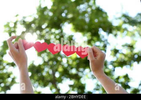 Weibliche Hände mit Kette von Papier Herzen über Natur Hintergrund Stockfoto