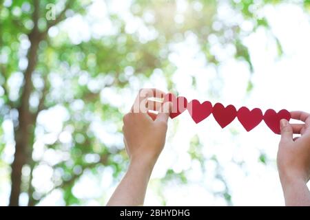 Weibliche Hände mit Kette von Papier Herzen über Natur Hintergrund Stockfoto