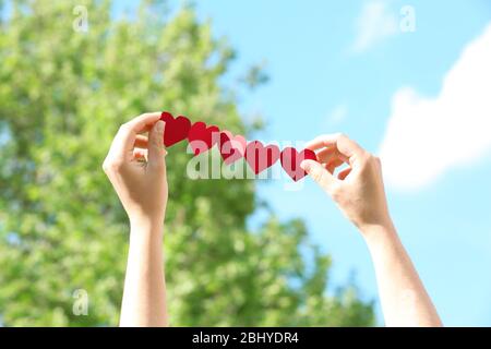 Weibliche Hände mit Kette von Papier Herzen über Natur Hintergrund Stockfoto