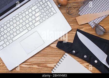 Verschiedene Küchenutensilien und Laptop der hölzerne Hintergrund, Draufsicht. Stockfoto