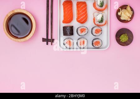 Frisches Sushi und Brötchen und Essstäbchen auf rosa Tisch, Stockfoto