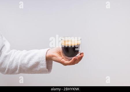 Frau Hand in weißen Bademantel hält Glas Doppel-Wand Tasse mit Espresso Stockfoto