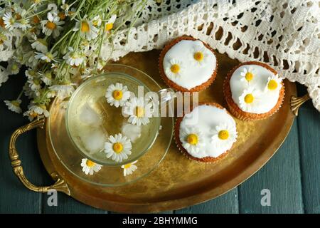 Tasse Kamille Tee mit Kamille Blumen und leckere Muffins auf Tablett, auf farbigen Holzhintergrund Stockfoto