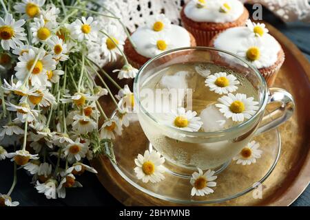 Tasse Kamille Tee mit Kamille Blumen und leckere Muffins auf Tablett, auf farbigen Holzhintergrund Stockfoto