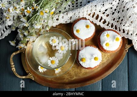 Tasse Kamille Tee mit Kamille Blumen und leckere Muffins auf Tablett, auf farbigen Holzhintergrund Stockfoto