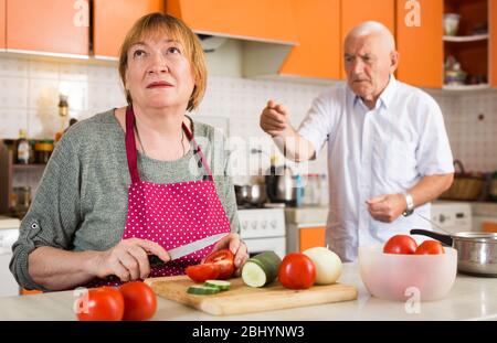 Ältere Frau beleidigte ihren Mann, der am Tisch in der Küche saß Stockfoto