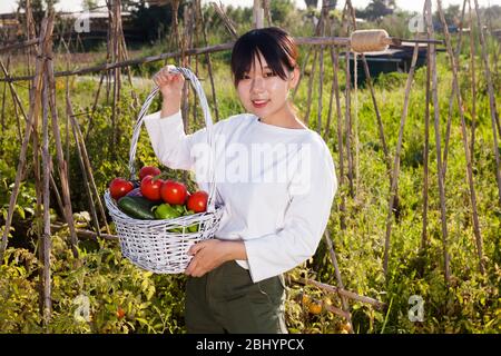 Portrait von jungen asiatischen Frau mit Korb voller geernteten Gemüse in Ihrem Garten Stockfoto
