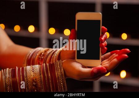 Junge Frau, die anlässlich von Diwali ein Mobiltelefon in den Händen hält. Stockfoto