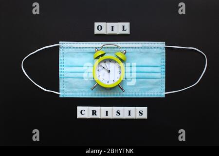 Phrase ÖLKRISE und Einweg-Maske mit Uhr auf schwarzem Hintergrund. Rückgang des Ölpreises, Marktrückgang. Konzept der Finanzkrise. Coronavirus, Stockfoto