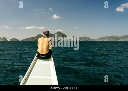 Mann auf dem Rücken auf dem Bug eines traditionellen philippinischen Bootes auf einem Inselhüpfen in El Nido, Palawan, Philippinen. Vertikal. Stockfoto