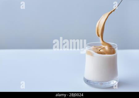 Koreanischer Dalgon-Kaffee. Minimalismus auf weißem Betonboom Hintergrund. Kopierbereich. Gesichtslos. Ein Löffel fügt Kaffeesahne hinzu. Stockfoto