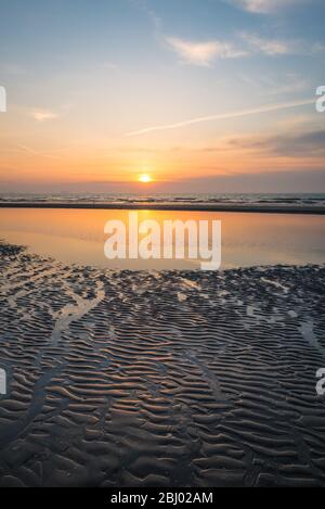 Farbenprächtiger Sonnenuntergang über der Nordsee, von der niederländischen Küste aus gesehen. Schönes Muster von Wellen und Wellen im nassen Sand. Stockfoto