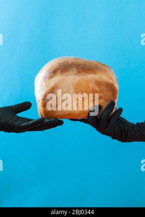 Die Hände mit schwarzen Handschuhen halten den Brotlaib. Stockfoto