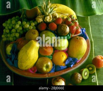 Schale mit exotischen frischen Früchten auf Hintergrund von Bananenblättern Stockfoto