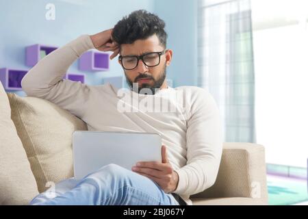 Junger Mann, der sich zu Hause auf dem Sofa entspannt und sein Tablet benutzt. Stockfoto