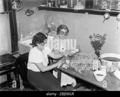 Miss Muriel Haken und Miss Irons schälen Zwiebeln, während sie eine Brille tragen, um sie zu stoppen weinen. - - 1938 - - Stockfoto