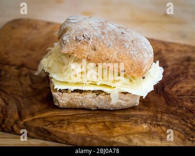 Nährendes Sandwich zum Mittagessen aus dünn geschnittenem Cheshire-Käse mit Sauerkraut auf braunem Ciabatta. (Glutenfreies Brot) Stockfoto