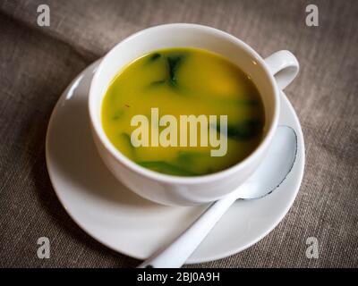 Leichte, frische Suppe aus Hummerbrühe mit Safran, Garnelen, Erbsen und Babyspinatblättern, serviert in einer großen Kaffeetasse. Stockfoto