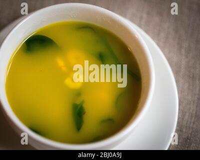 Leichte, frische Suppe aus Hummerbrühe mit Safran, Garnelen, Erbsen und Babyspinatblättern, serviert in einer großen Kaffeetasse. Stockfoto