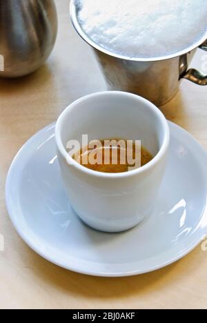 Weiße Porzellanbecher frisch gebrühter Espresso mit Crema und Milchschaum in Kanne und Kakaobecher - der Espresso wird zu capp Stockfoto