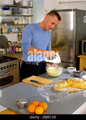 Gary Rhodes in der heimischen Küche, der Zutaten für ein festliches Brot und Butterpudding zuflüstert - Stockfoto