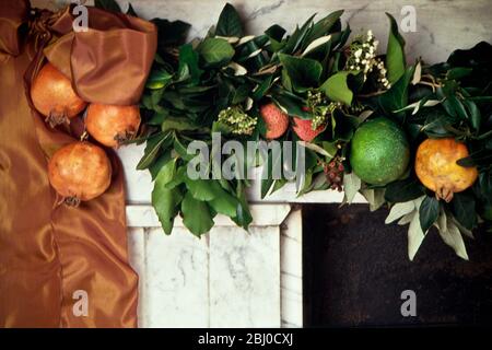 Opulenter Kaminstückchen aus reichen Bändern und frischen Früchten mit natürlichem Grün auf altem Marmormantelstück. - Stockfoto