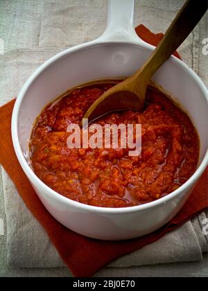 Tonato-Sauce in einem weißen Keramikkochtopf unter Rühren mit einem Holzlöffel - Stockfoto