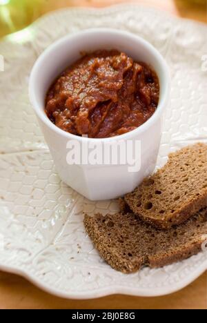 Weißer Topf mit getrockneten Tomatenpastete als Dip mit grobem Roggenbrot. - Stockfoto