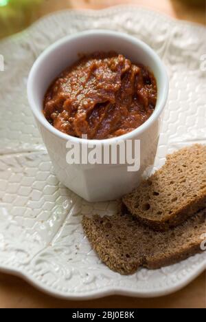 Weißer Topf mit getrockneten Tomatenpastete als Dip mit grobem Roggenbrot. - Stockfoto