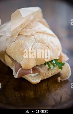 Italienische Schinken Sandwich, parma Schinken, Mozzarella Käse, und frech Rakete auf Licht Ciabatta Art Brot, in fettfreien Papier verpackt. - Stockfoto