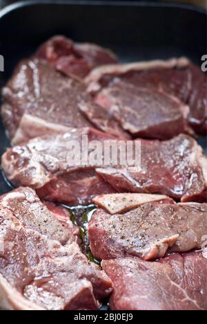 Stücke von Rumpsteak, die in Olivenöl, Rotwein und schwarzem Pfeffer mariniert werden - Stockfoto