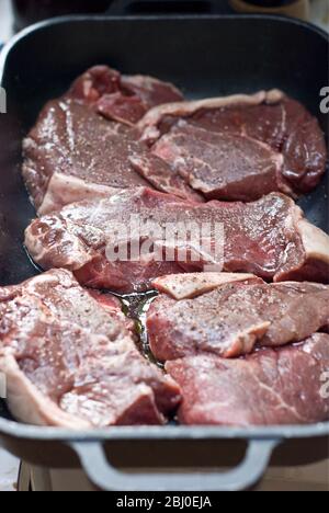 Stücke von Rumpsteak, die in Olivenöl, Rotwein und schwarzem Pfeffer mariniert werden - Stockfoto