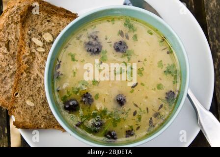 Schüssel mit Hühnersuppe mit zypriotischen Trahanas, violettem, sprießenden Brokkoli und gehackter Petersilie, mit Roggenbrot mit Vollkornkrone an der Seite. - Stockfoto