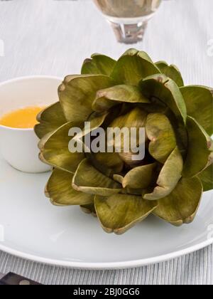 Ganze gekochte Globe Artischocke auf weißem Teller mit Topf geschmolzener Butter serviert - Stockfoto