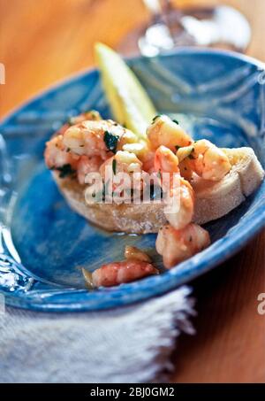 Große mediterrane Garnelen in Knoblauch und Olivenöl mit Koriander auf Ciabatta Brot mit Zitronenkeil auf blauer Platte geworfen - Stockfoto