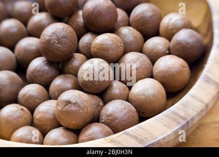 Ganze Macadamianüsse in ihren Schalen in Holzschale - Stockfoto