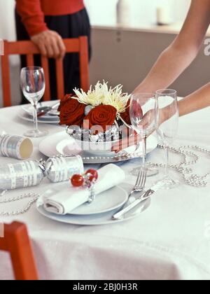 Weihnachtliche Tischdekoration aus tiefroten Rosen und stacheligen Chrysanthemen mit silbernen Kugeln, die auf den Tisch gestellt werden - Stockfoto