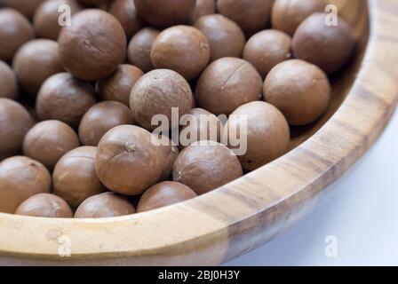 Ganze Macadamianüsse in ihren Schalen in Holzschale - Stockfoto