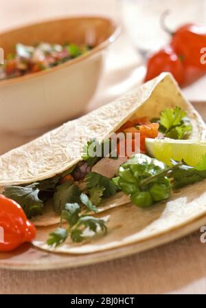 Tortilla aus weichem Mehl mit Huhn und Salsa serviert mit Limettenkeilen und scharfen roten und grünen schottischen Bonnet Chili Paprika - Stockfoto