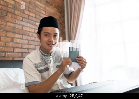 Asiatische muslimische Männer tragen Mütze, wenn sie einen Pass nach der Vorbereitung eines Koffers halten Stockfoto