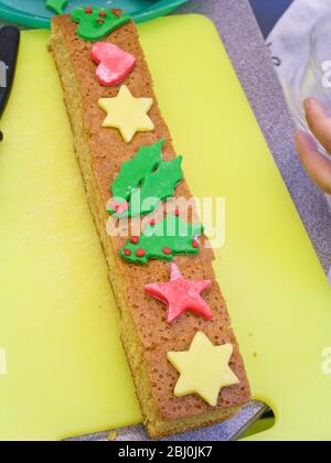 Kinder schneiden dekorative Weihnachtsformen aus farbigen Fondant Vereisung Kuchen dekorieren - Stockfoto