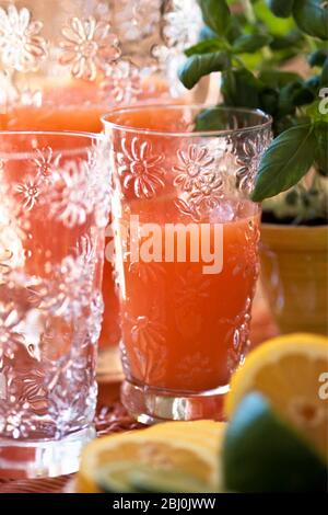 Rosa Grapefruit oder gemischter Beakfast Saft in dekorativem Glas und Krug mit geschnittenen Zitronen und Limetten - Stockfoto
