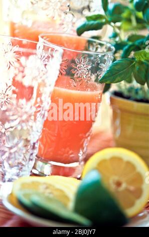 Rosa Grapefruit oder gemischter Beakfast Saft in dekorativem Glas und Krug mit geschnittenen Zitronen und Limetten - Stockfoto
