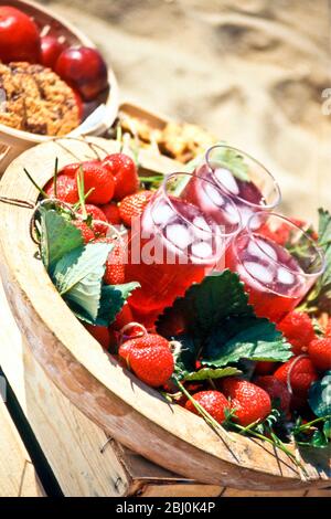 Erdbeersaft in hohen Gläsern mit Eis auf Tablett mit Erdbeeren und Erdbeerblättern verziert - Stockfoto