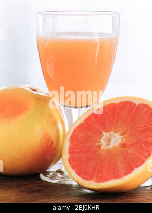 Frische ganze rosa Grapefruits mit einem Glas Grapefruitsaft - Stockfoto