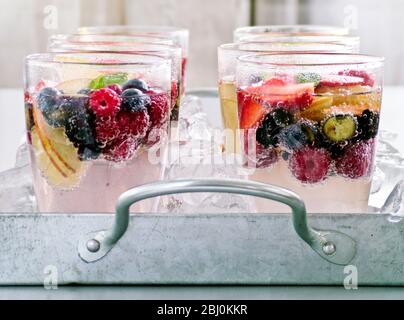 Mineralwasser mit frischem Obst und Beeren in Gläsern auf zerdrücktem Eis auf Metalltablett - Stockfoto