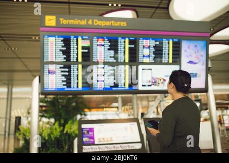 Passagiere, die am Fluginformationsbrett im Wartebereich des Flughafenterminals reisen, prüfen die Zeit für Abflug-Ankunft und den Flugstatus für Verspätungen Stockfoto