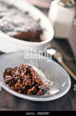 Portion heißer Schokoladenpudding auf Glasplatte mit ganzer Pudding im Hintergrund - Stockfoto