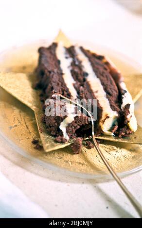 Reichhaltige Schokoladenkuchen mit Schichten von Buttercreme auf sternförmigen Teller mit Dessertgabel serviert - Stockfoto