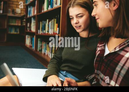 Studentinnen in der Bibliothek. Junge Leute sitzen zusammen auf dem Boden in der Bibliothek mit Büchern und Laptop für die Recherche Informationen für ihre Stockfoto